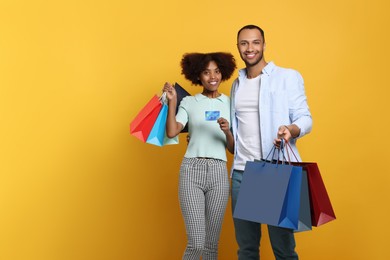 Photo of Happy African American couple with shopping bags and credit card on orange background. Space for text