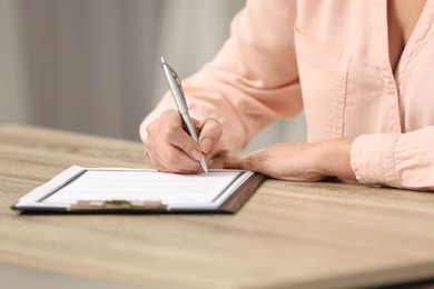 Senior woman signing Last Will and Testament at wooden table indoors, closeup