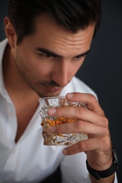 Young man with glass of whiskey on dark background