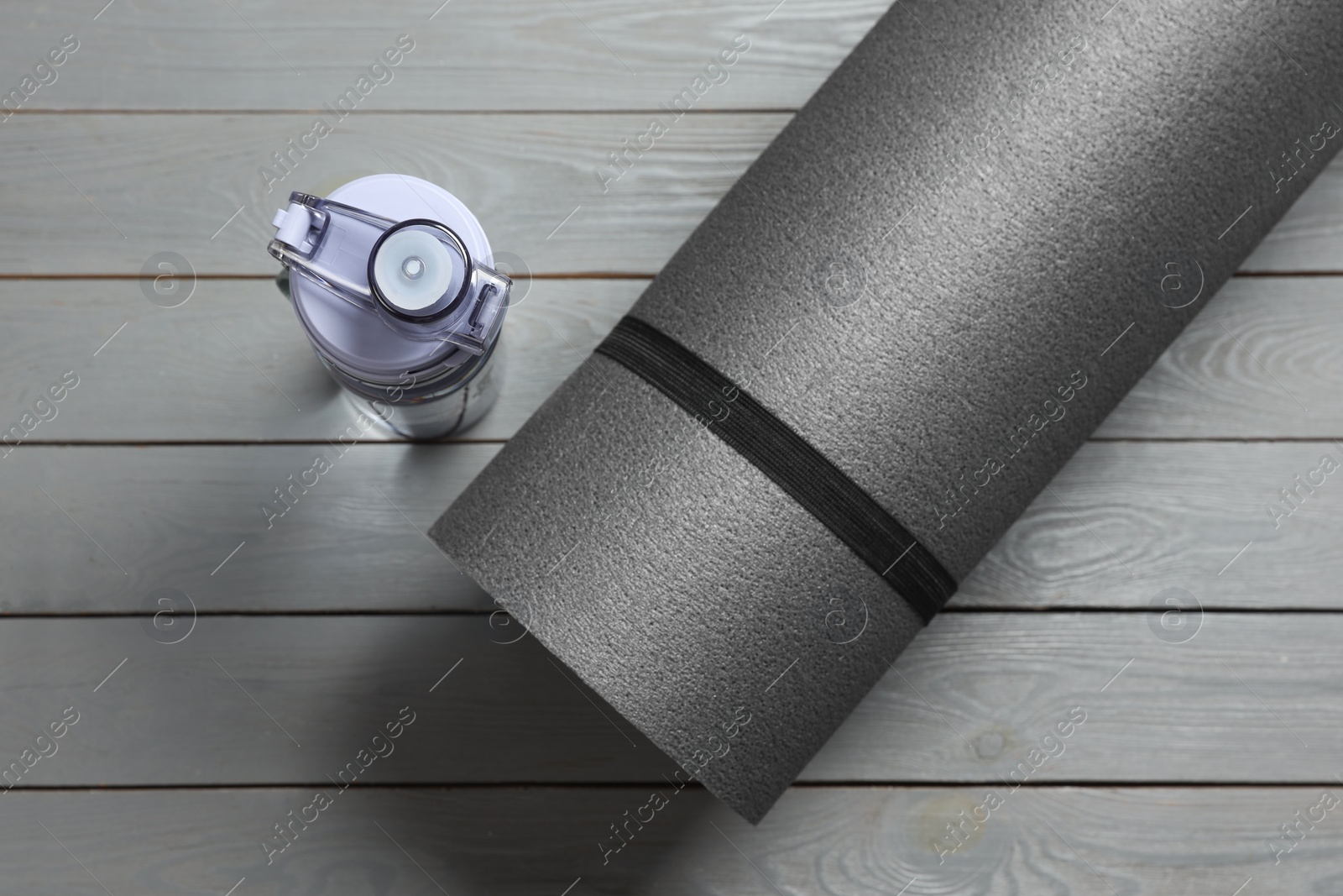 Photo of Yoga mat and bottle of water on grey wooden floor, flat lay