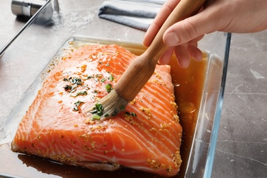 Photo of Woman marinating raw salmon in dish at table