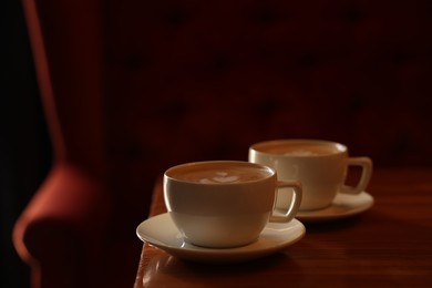 Photo of Cups of aromatic coffee with foam on wooden table in cafe