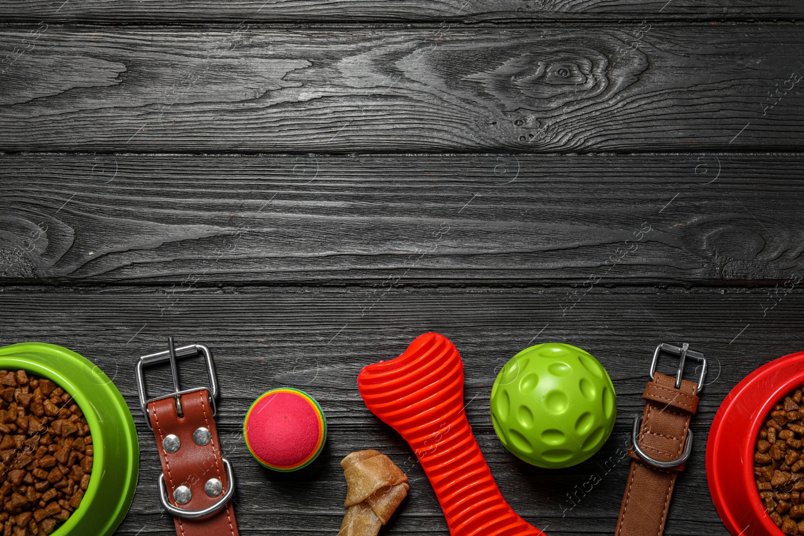 Photo of Flat lay composition with dog collars, toys and food on black wooden table. Space for text