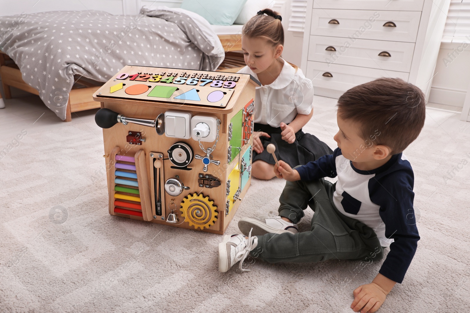 Photo of Little boy and girl playing with busy board house on floor in room