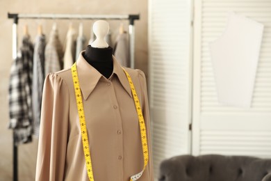 Photo of Mannequin with shirt and measuring tape in tailor shop, space for text