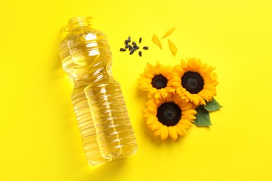 Bottle of cooking oil, sunflowers and seeds on yellow background, flat lay