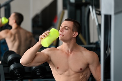 Athletic young man drinking protein shake in gym