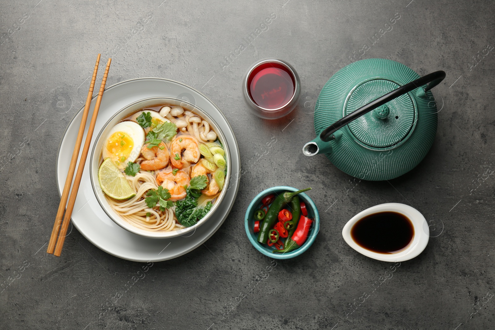 Photo of Delicious ramen with shrimps and egg in bowl served on grey table, flat lay. Noodle soup