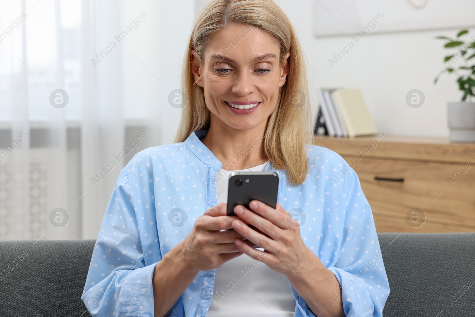 Photo of Happy woman sending message via smartphone at home