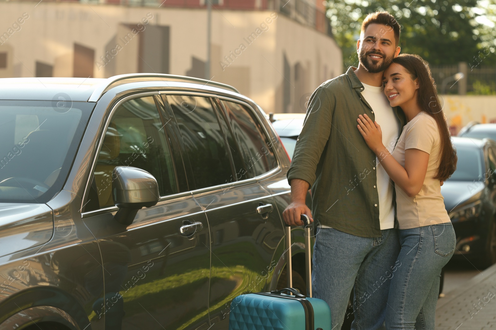 Photo of Long-distance relationship. Beautiful young couple with suitcase hugging near car outdoors