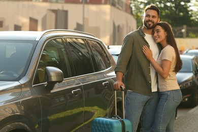 Long-distance relationship. Beautiful young couple with suitcase hugging near car outdoors