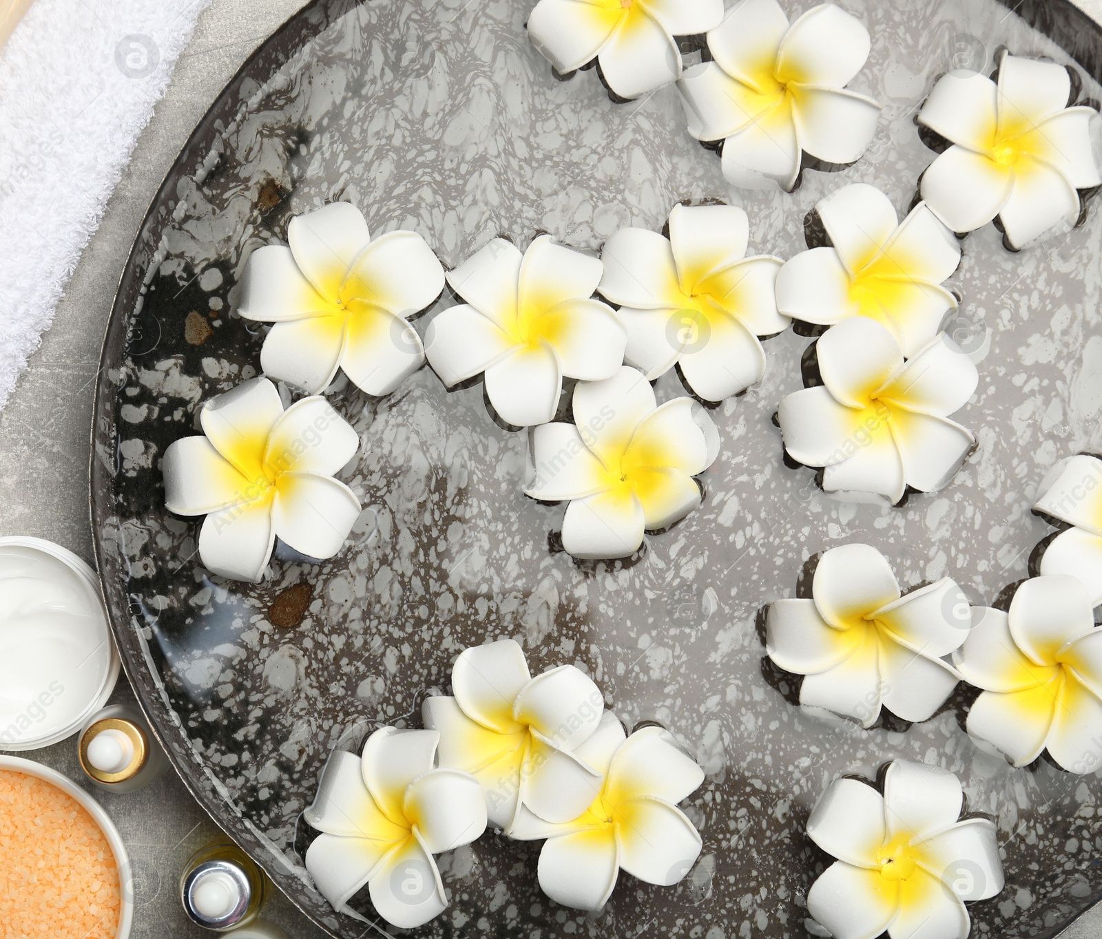 Photo of Bowl of water with flowers and different spa supplies on light grey table, flat lay