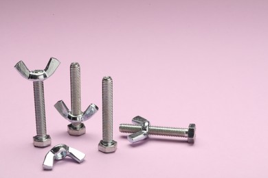 Metal screws with wing nuts on purple background, space for text