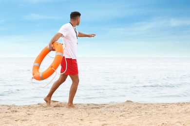 Photo of Handsome male lifeguard with life buoy at sandy beach