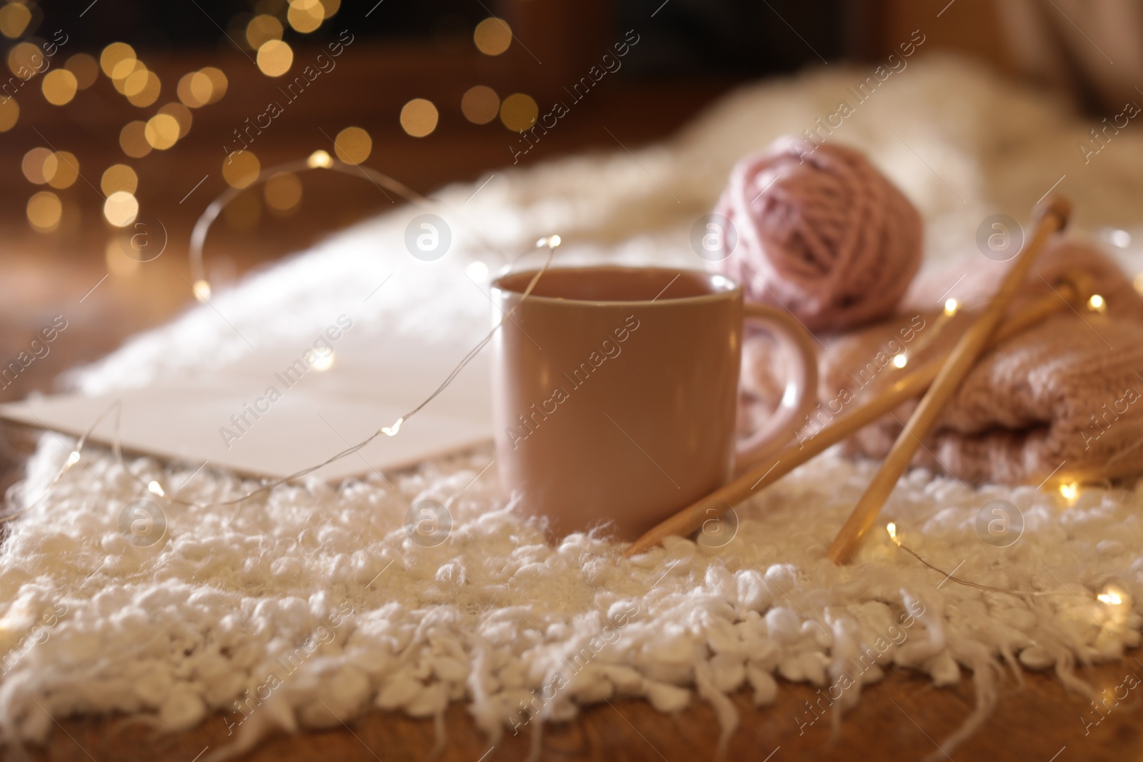 Photo of Composition with cup of hot beverage, knitting yarn and book on fuzzy rug. Winter evening