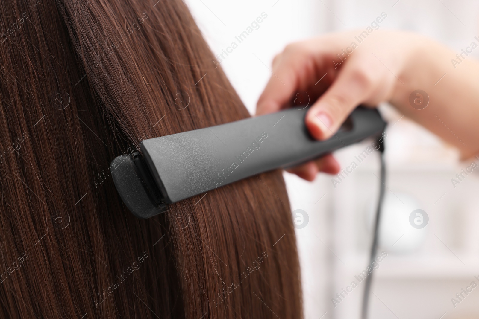 Photo of Hairdresser straightening woman's hair with flat iron in salon, closeup