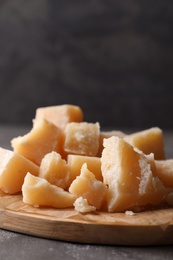 Parmesan cheese with wooden board on grey table, closeup