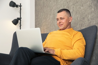 Photo of Mature man working with laptop on sofa indoors