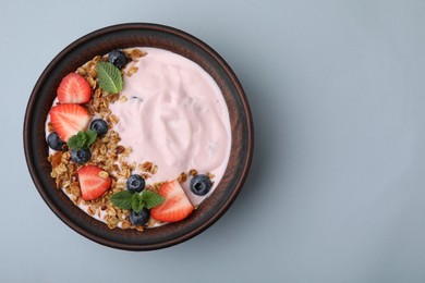 Bowl with yogurt, berries and granola on light grey background, top view. Space for text