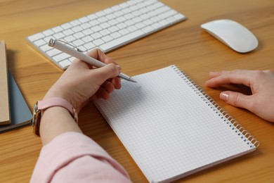 Photo of Left-handed woman writing in notebook at wooden desk, closeup