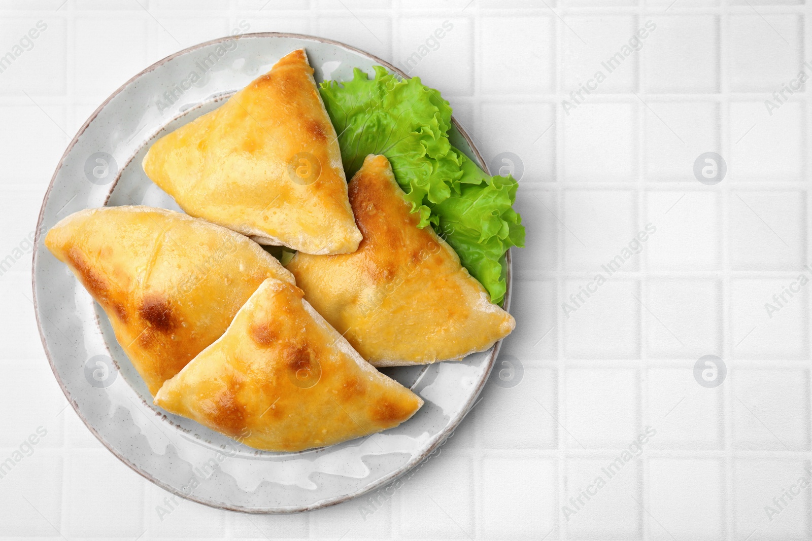 Photo of Delicious samosas and lettuce on white tiled table, top view. Space for text