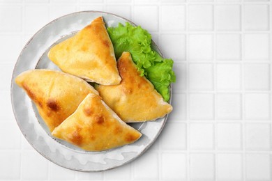 Photo of Delicious samosas and lettuce on white tiled table, top view. Space for text