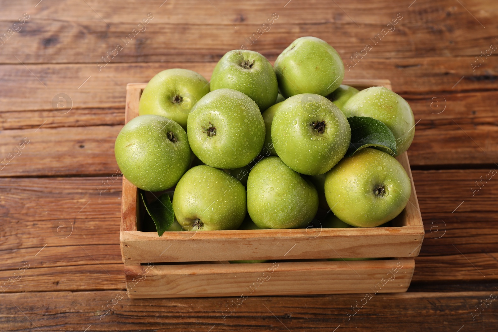 Photo of Fresh ripe green apples with water drops in crate on wooden table