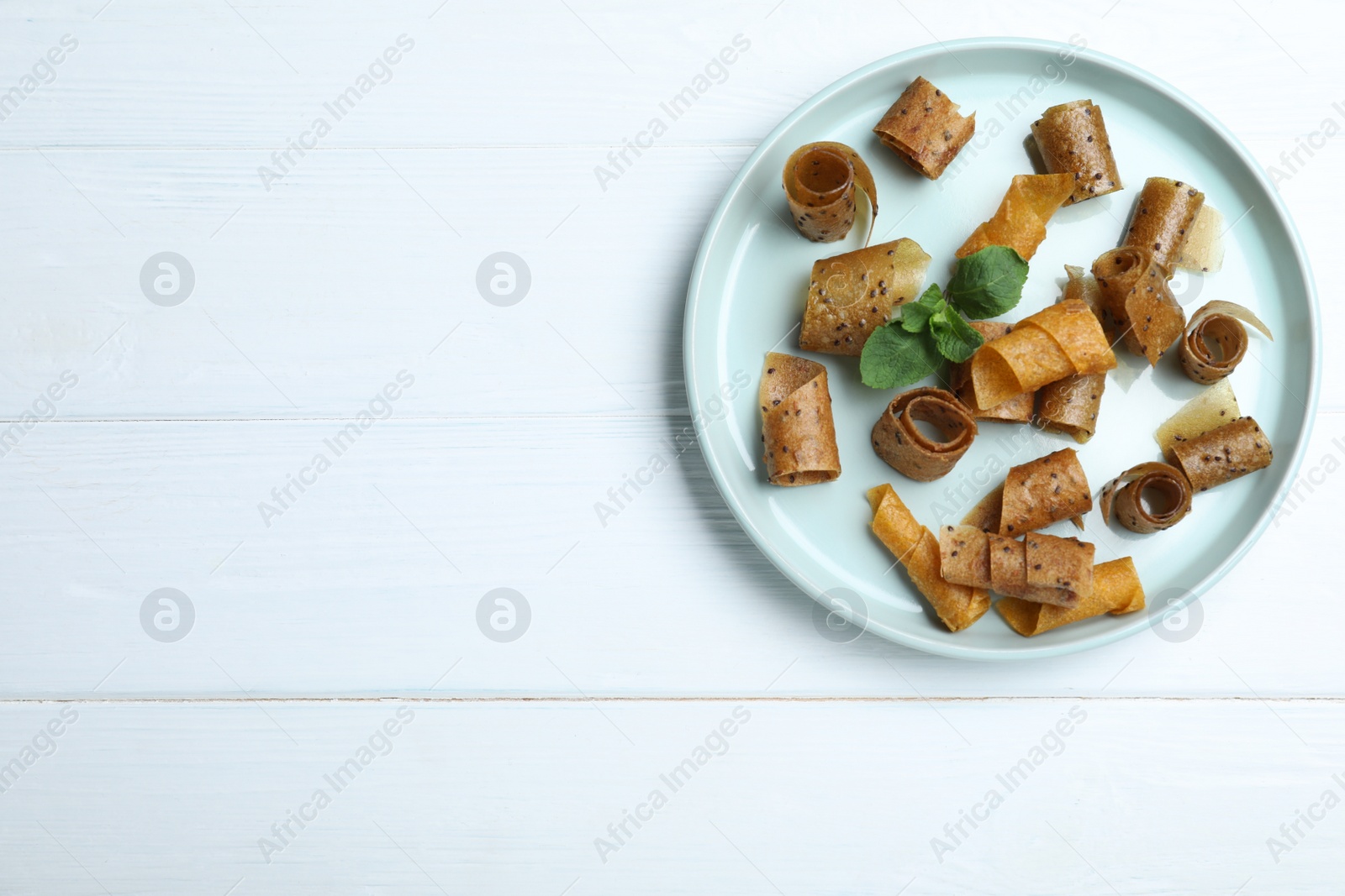 Photo of Delicious fruit leather rolls on white wooden table, top view. Space for text