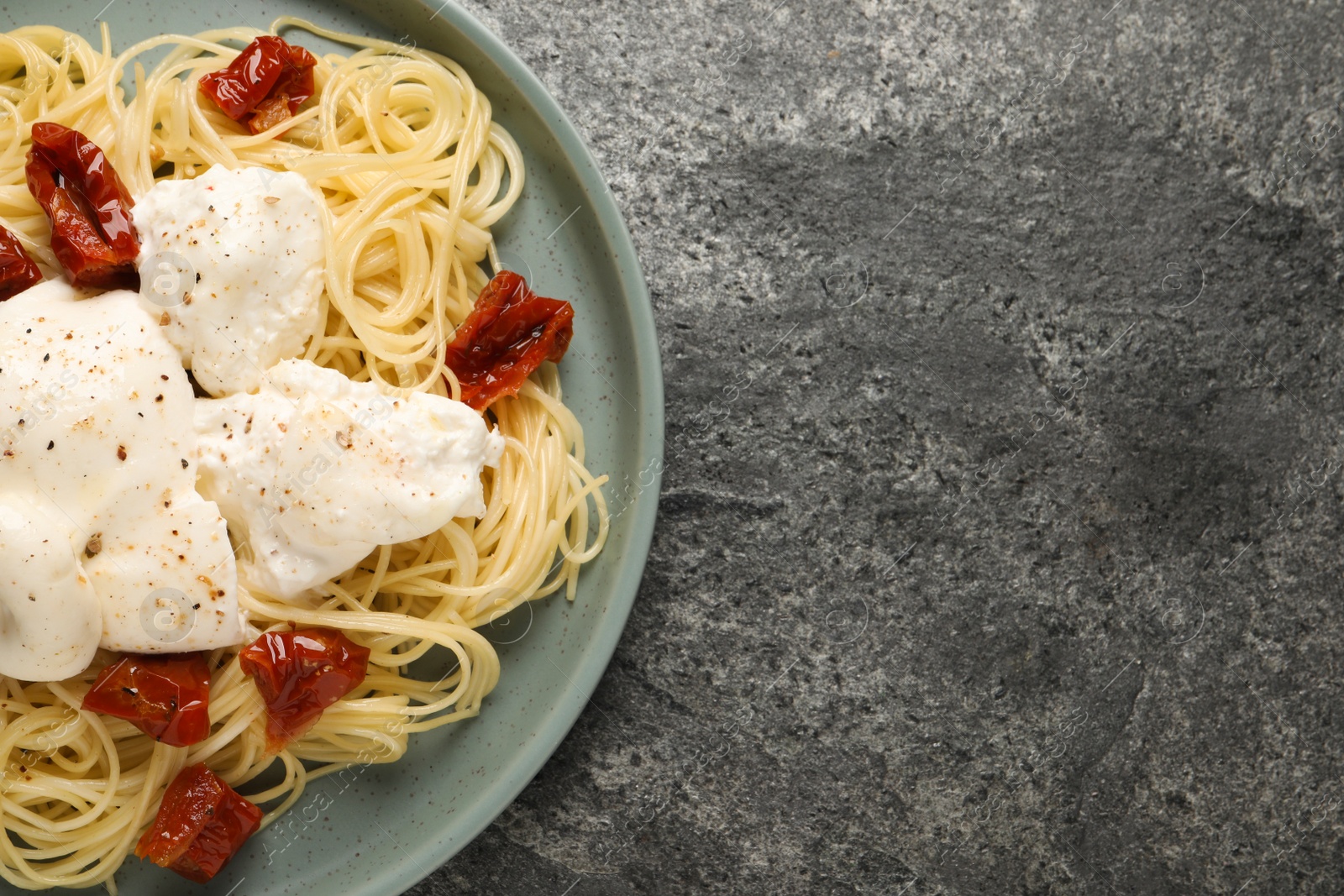 Photo of Delicious spaghetti with burrata cheese and sun dried tomatoes on grey table, top view. Space for text