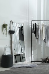 Photo of Rack with stylish women's clothes and large mirror in dressing room. Interior design