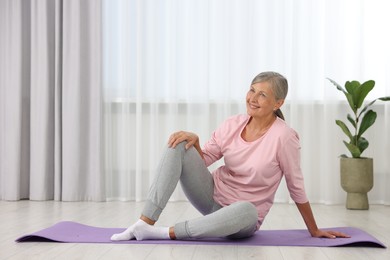 Photo of Happy senior woman sitting on mat at home, space for text. Yoga practice