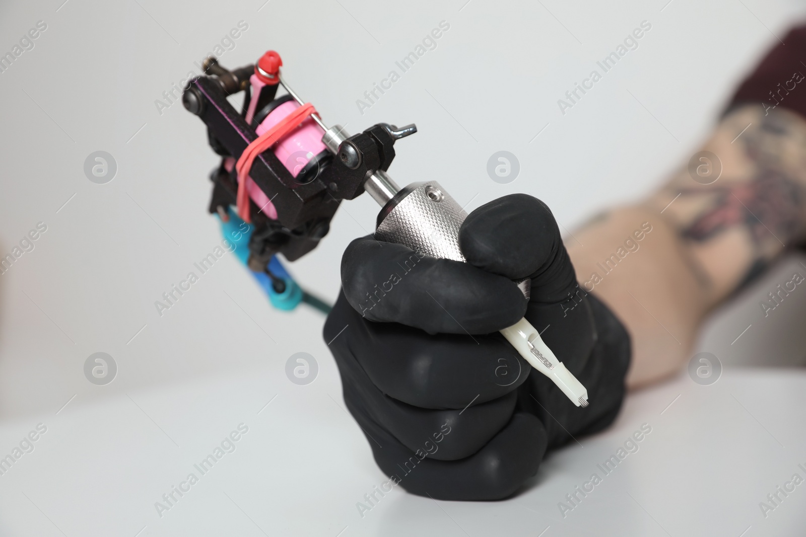 Photo of Tattoo artist with professional machine at table against light background, closeup