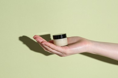 Woman holding jar of cream on green background, closeup