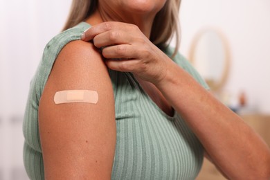 Photo of Woman with adhesive bandage on her arm after vaccination against blurred background, closeup