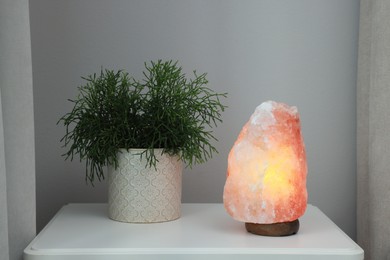 Photo of Beautiful Himalayan salt lamp and green houseplant on white table in room