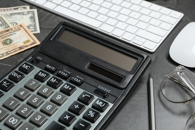 Photo of Calculator, glasses, money and keyboard on dark grey table, closeup. Tax accounting