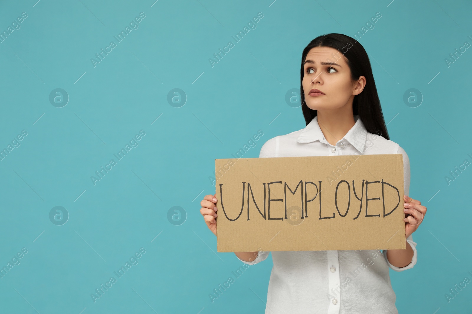 Photo of Unhappy woman holding sign with word Unemployed on light blue background. Space for text