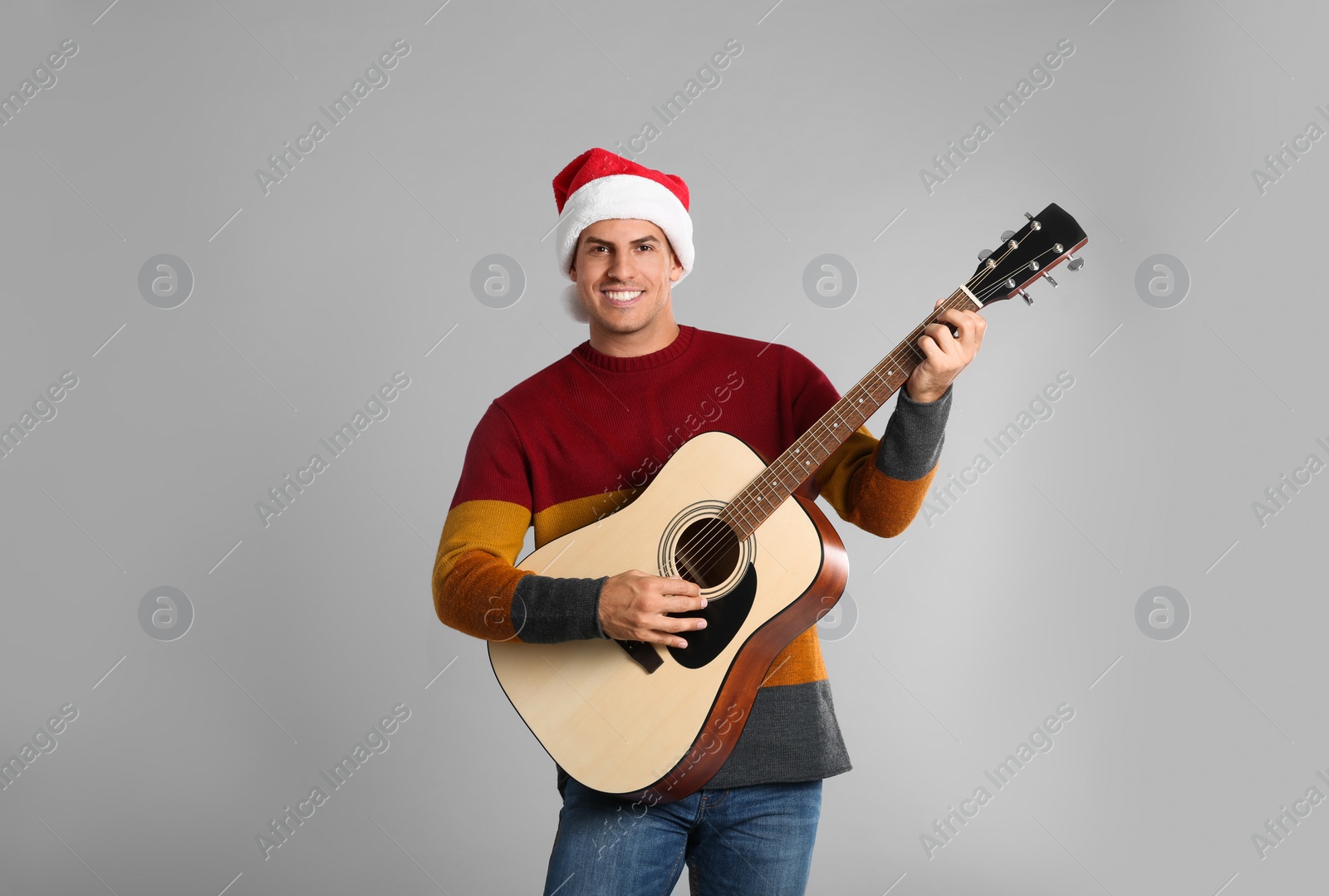 Photo of Man in Santa hat playing acoustic guitar on light grey background. Christmas music