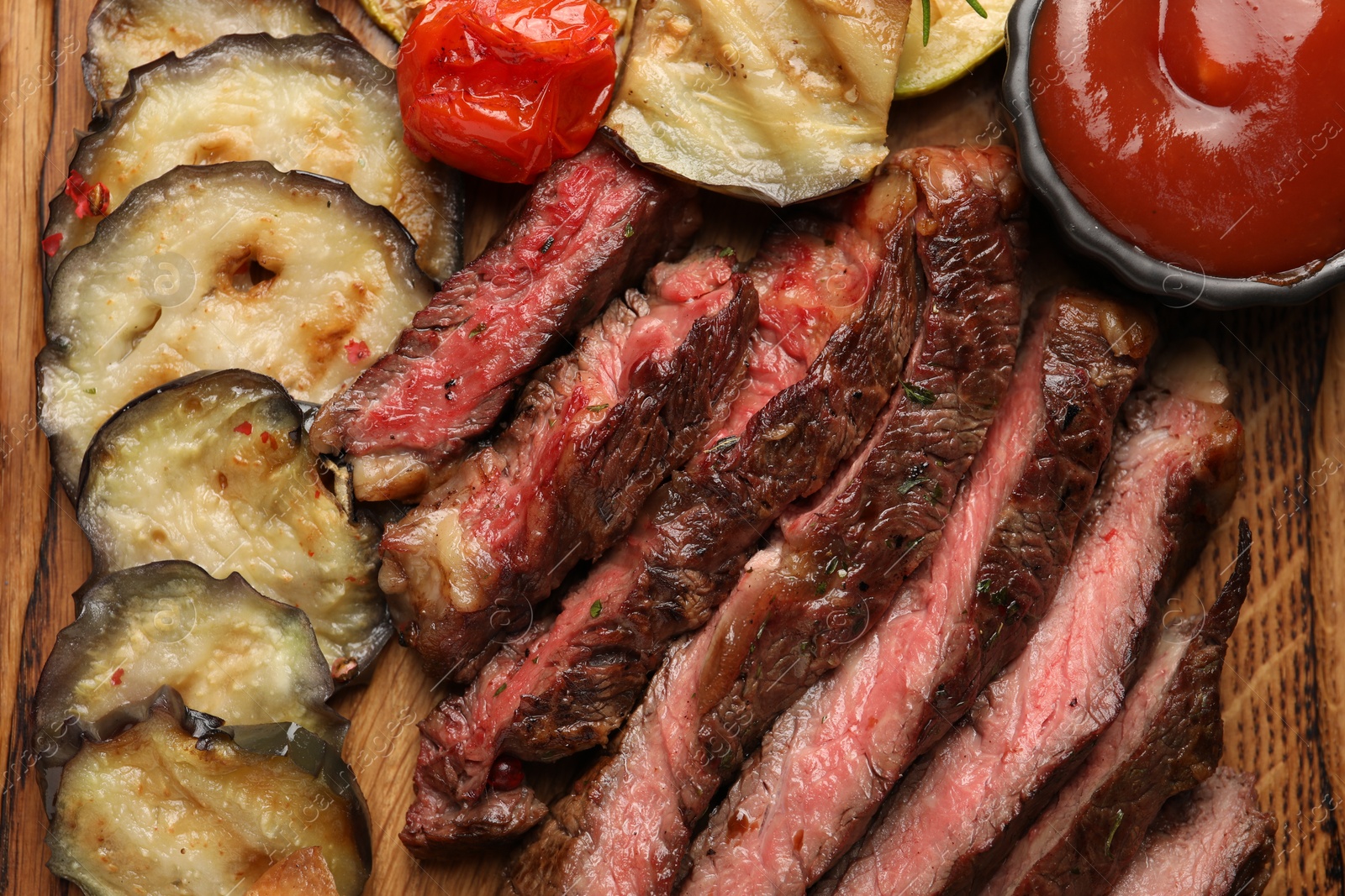 Photo of Delicious grilled beef with vegetables and tomato sauce on wooden table, top view