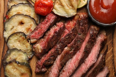 Delicious grilled beef with vegetables and tomato sauce on wooden table, top view