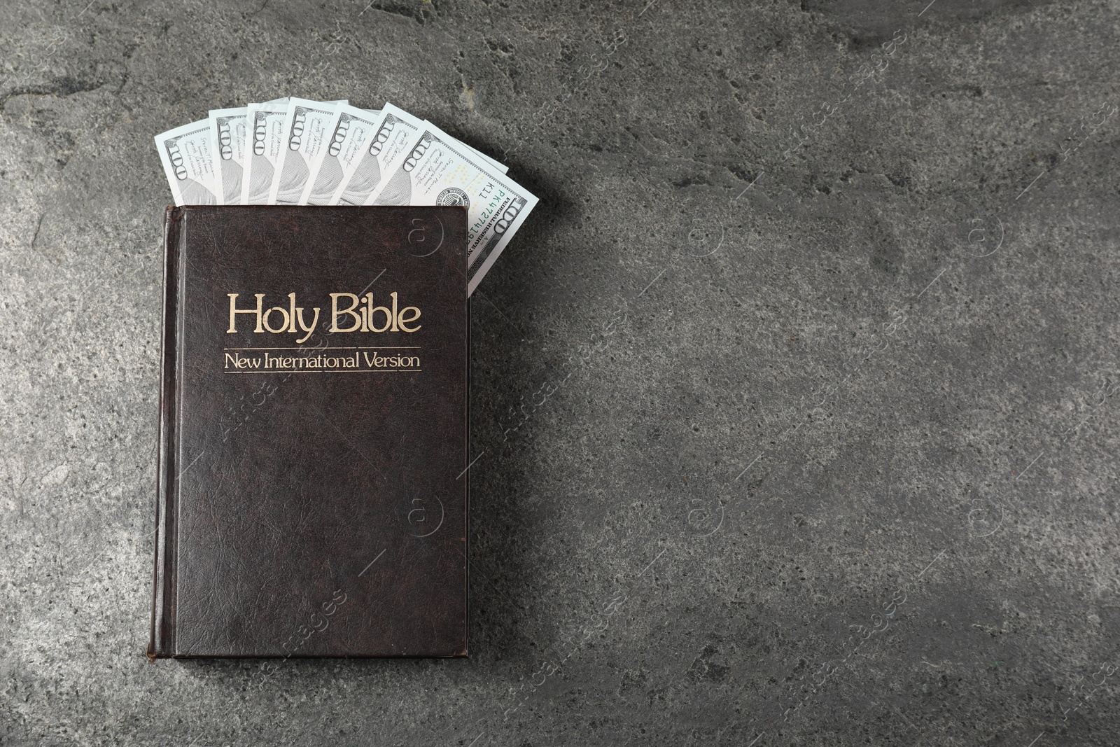 Photo of Holy Bible and money on grey table, top view. Space for text