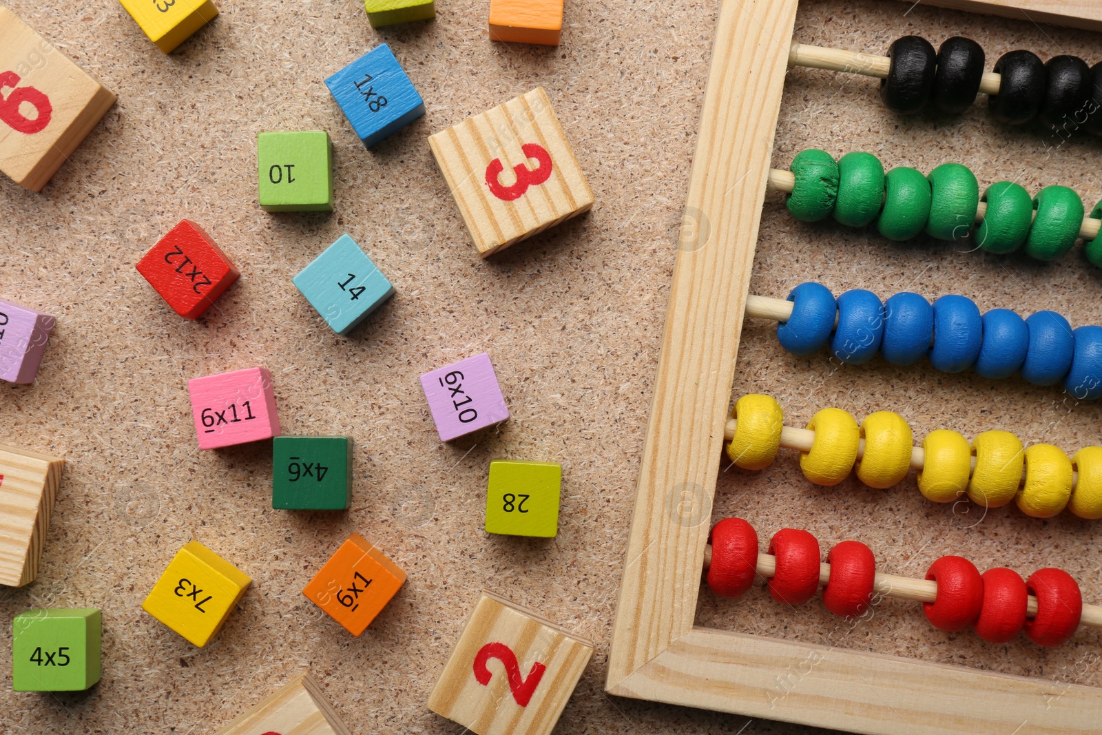 Photo of Wooden cubes with numbers and multiplications near abacus on fiberboard, flat lay