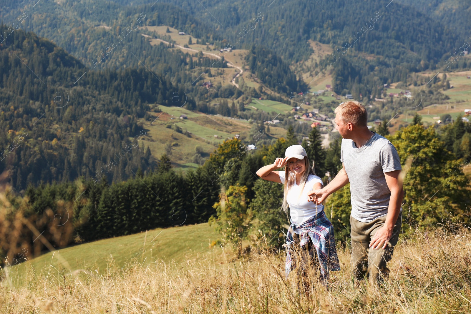 Photo of Couple going up grassy hill surrounded by beautiful nature. Space for text