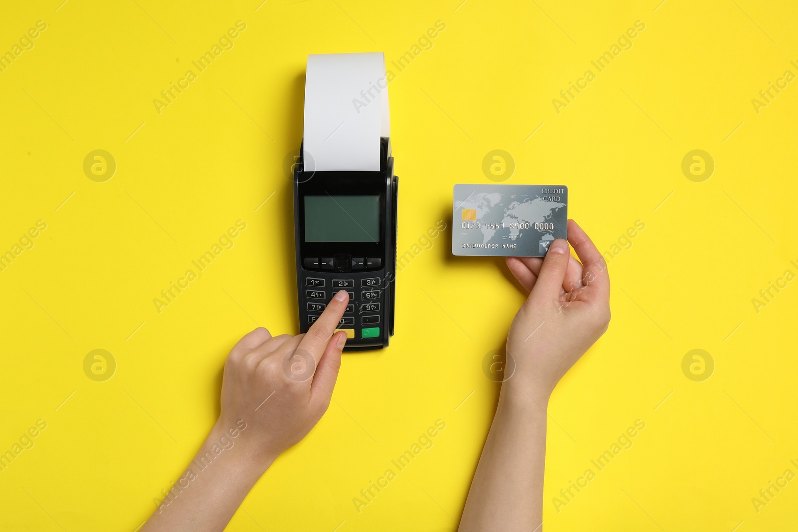 Photo of Woman using payment terminal with credit card and thermal paper for receipt on yellow background, top view