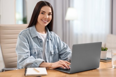 Photo of Young woman watching webinar at table in room