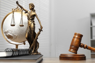 Figure of Lady Justice, gavel, notebooks and globe on table indoors, space for text. Symbol of fair treatment under law