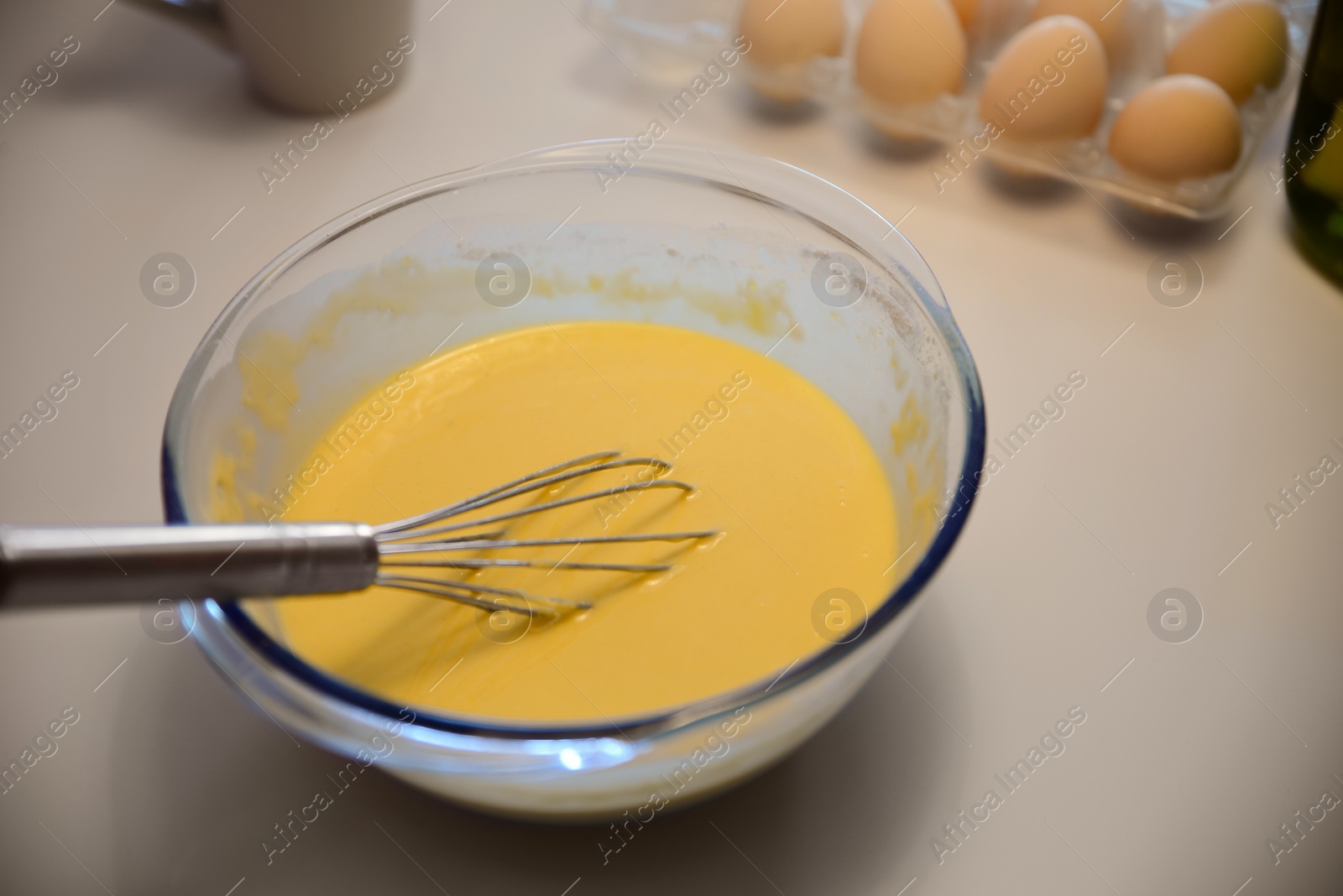 Photo of Glass bowl of crepe batter with whisk on white table, closeup