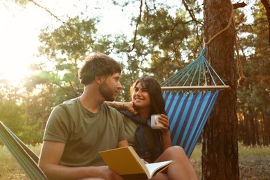 Lovely couple with book resting in comfortable hammock outdoors