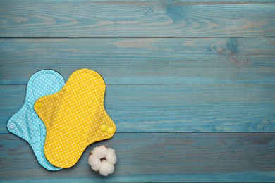 Photo of Reusable cloth menstrual pads and cotton flower on light blue wooden table, flat lay. Space for text