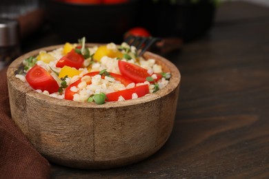 Photo of Cooked bulgur with vegetables in bowl on wooden table, closeup. Space for text